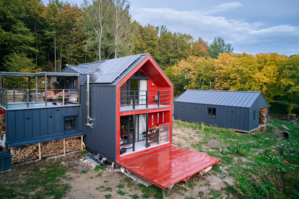 Modern prefab steel building in Canada with blue-gray siding, white trim, and a large garage door, surrounded by evergreen trees and cloudy sky.